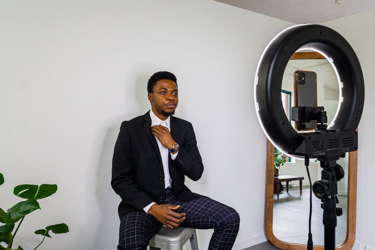 Young man adjusts outfit for a vlog in a modern setup with smartphone and ring light.