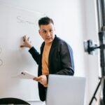 A male teacher explains math equations on a whiteboard during an online class.