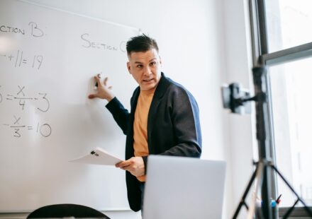 A male teacher explains math equations on a whiteboard during an online class.