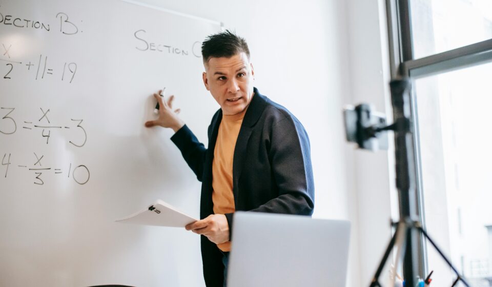 A male teacher explains math equations on a whiteboard during an online class.