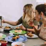 Two women enjoying a diverse selection of Asian dishes at a dining table indoors.