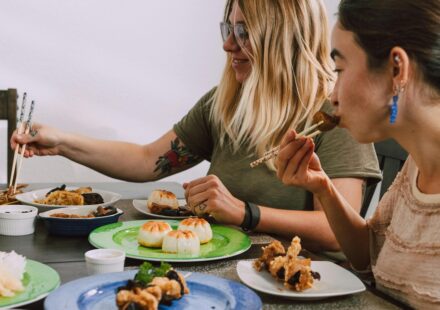 Two women enjoying a diverse selection of Asian dishes at a dining table indoors.