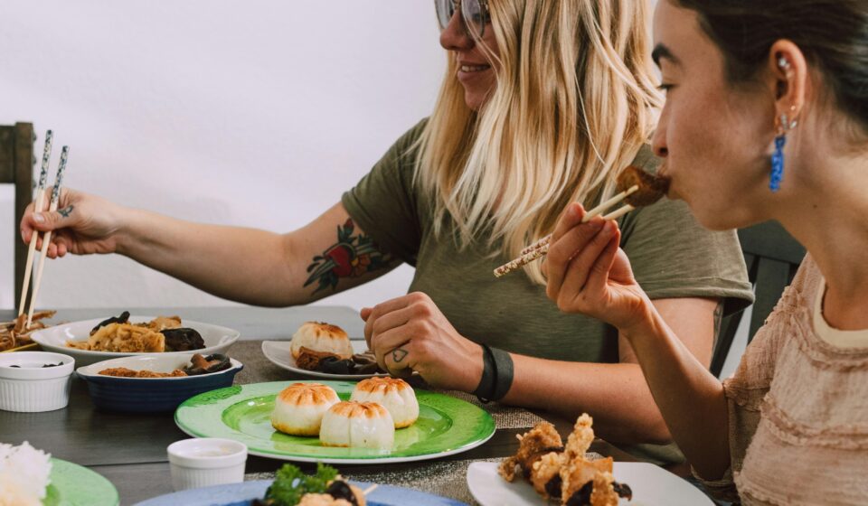 Two women enjoying a diverse selection of Asian dishes at a dining table indoors.