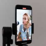 A woman records a makeup tutorial using a smartphone on a gimbal, capturing content for social media.