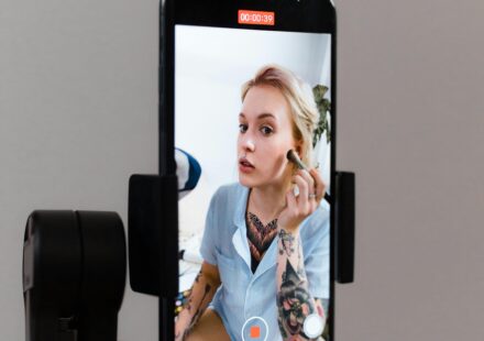 A woman records a makeup tutorial using a smartphone on a gimbal, capturing content for social media.