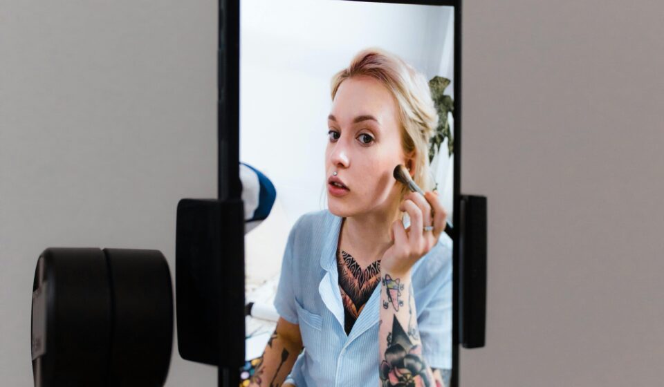 A woman records a makeup tutorial using a smartphone on a gimbal, capturing content for social media.